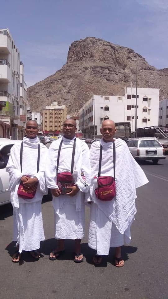 Tiga peserta berpakaian ihram bergambar dengan latar bukit